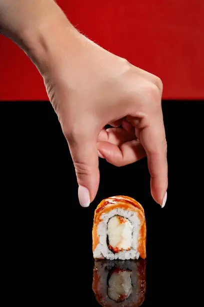 Photo of Female hand taking uramaki roll with seared salmon, cream cheese, tobiko and apple