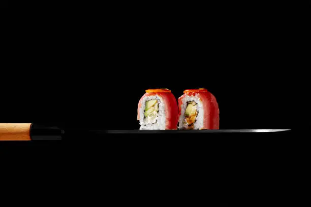 Photo of Uramaki rolls with tuna, cream cheese, avocado and kumquat slices on blade of Japanese sashimi knife