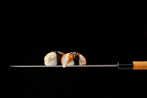 Photo of Nigiri sushi with eel served on blade of traditional Japanese knife on black background