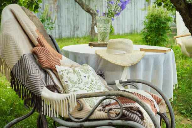 istock serene backyard, a rocking chair with a blanket invites relaxation, paired with a table hosting bluebells, a straw hat, and a book. A tranquil escape from urban chaos. 1703881007
