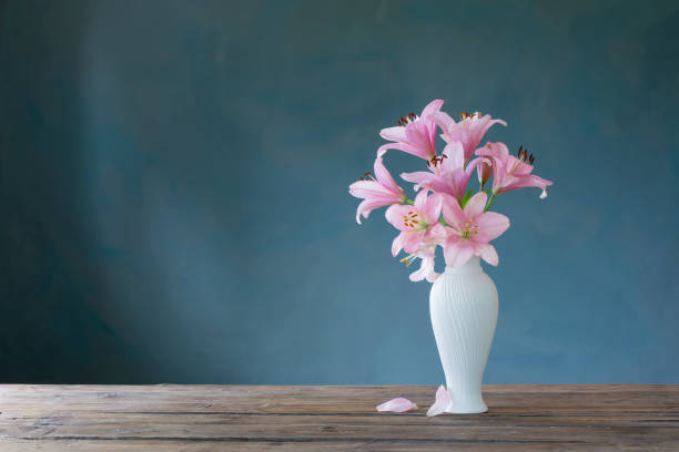 istock pink lily in white vase on blue background 1703884875