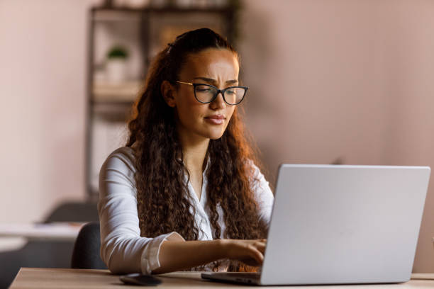istock Young woman with eyeglasses working at her desk, using laptop 1703892561