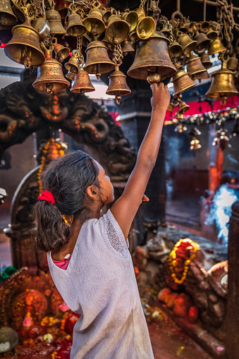 Portrait of young Nepali girl praying in an ancient temple in Bhaktapur. Bhaktapur is an ancient town in the Kathmandu Valley and is listed as a World Heritage Site by UNESCO for its rich culture, temples, and wood, metal and stone artwork.