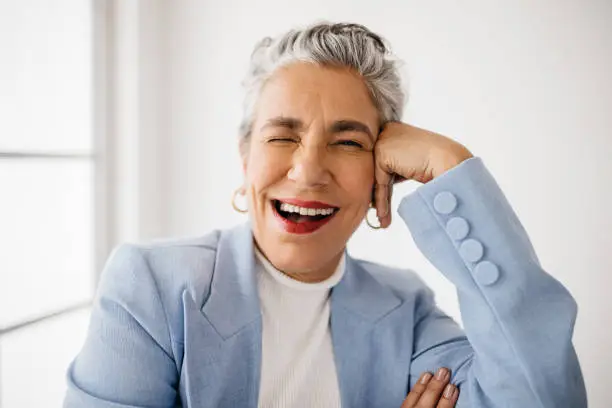 Senior female professional winking at the camera, sitting in her office in classy business attire. Mature business woman having fun at work, enjoying herself as an accomplished business person.
