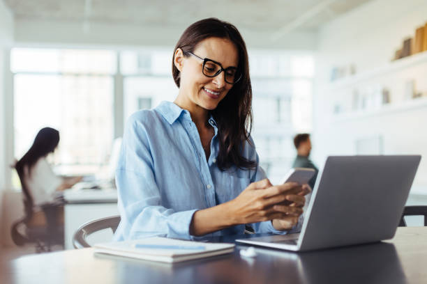 istock Happy business woman using a mobile phone while sitting in an office 1703910598