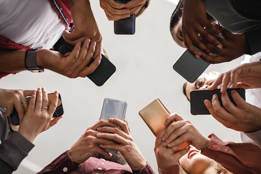 Directly below shot of unrecognizable group of diverse people standing in a circle and using their smart phones.