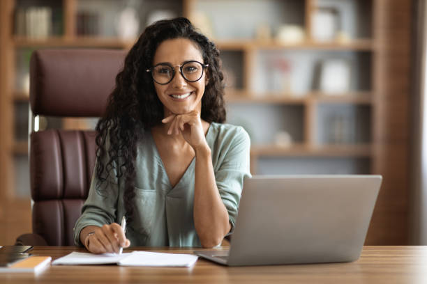 istock Positive young brunette woman using laptop at office 1703935334