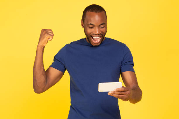 istock Joyful African American Man Using Phone Gesturing Yes, Yellow Background 1703935917