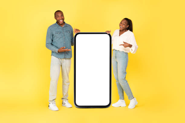 istock African Couple Pointing At Cellphone With Large Screen, Yellow Background 1703937135