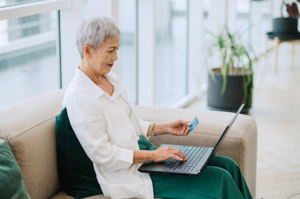 istock A Smiling Beautiful Elegant Senior Woman Using Her Credit Card and Her Computer While Relaxing at Home. 1703955104