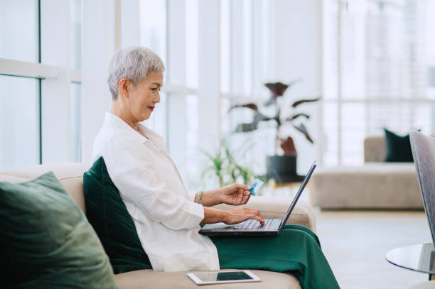 A Smiling Beautiful Elegant Senior Woman Using Her Credit Card and Her Computer While Relaxing at Home.