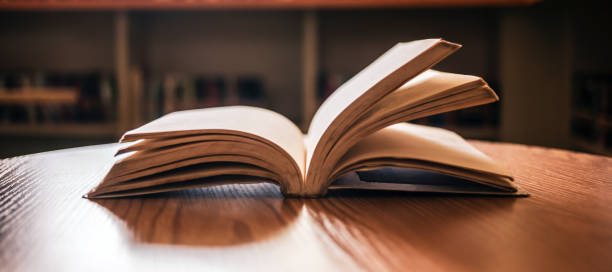 istock Vintage style.An open book or textbook vintage style in the library with light from the window on the reading table and the corridor of the bookshelves in the school classroom background.Education learning concept 1703961129