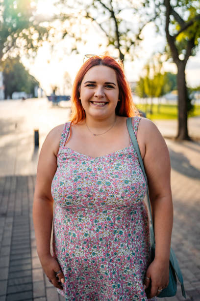 Young Woman Standing In The Park Portrait of a beautiful young plus size woman standing in the park. plus size woman fashion laughing stock pictures, royalty-free photos & images