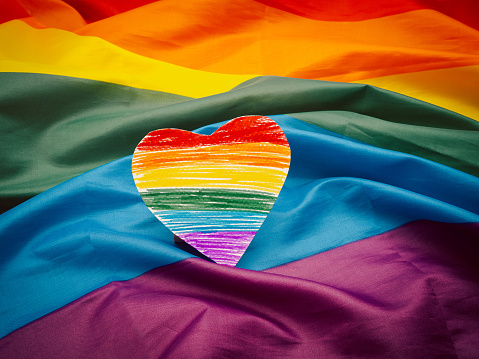 A rainbow heart shape symbol made from paper over the rainbow flag or LGBT flag. Pride month. LGBTQ concept