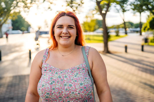 Young Woman Standing In The Park Portrait of a beautiful young plus size woman standing in the park. plus size woman fashion laughing stock pictures, royalty-free photos & images