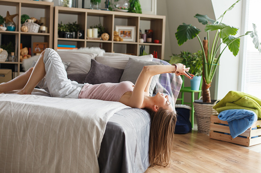 Portrait of happy young woman lying on back on her cozy bed and using digital tablet in the morning.