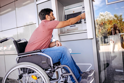 Young man in wheelchair inserting credit card in ATM for picking up cash