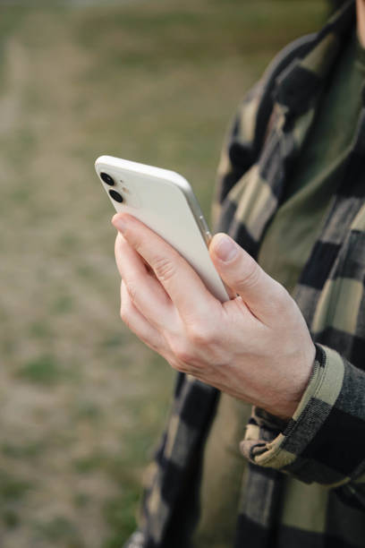 istock Man using white smartphone on blurred nature background, close up. 1703981879