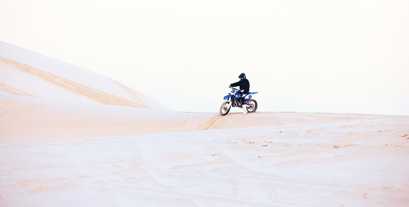 Desert, hill or athlete driving motorcycle for action, adventure or fitness with performance or adrenaline. Sand, sports or person on dirt motorbike on dunes for training, exercise or race challenge