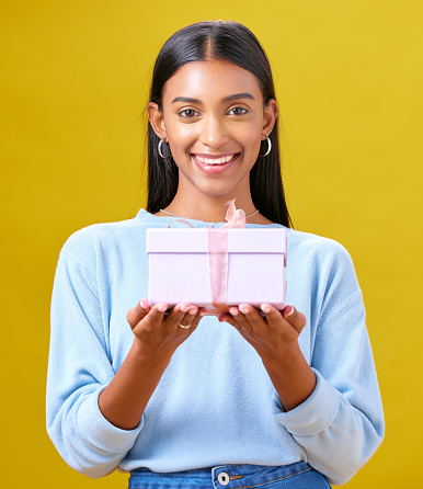 Woman, winner portrait and gift box, offer and prize for giveaway or shopping on yellow background. Happy person with present and ribbon package for retail sale, winning or competition in studio