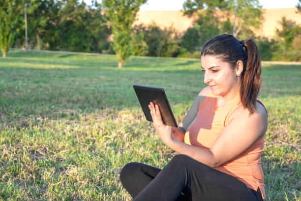 istock Young Caucasian woman smiling and happy using tablet sitting in park 1704040257