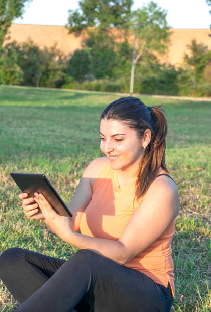istock Young Caucasian woman smiling and happy using tablet sitting in park 1704041931