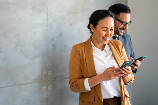 Middle aged asian business woman on the phone at office. Successful female texting on the mobile phone and working. Smiling businesswoman.