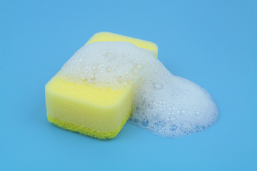 Yellow sponge with foam on blue background. Washing and cleaning concept.
