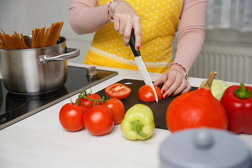 Close-up of woman preparing lunch. Chopping tomatos, peppers and other vegetables to make a souce for pasta.