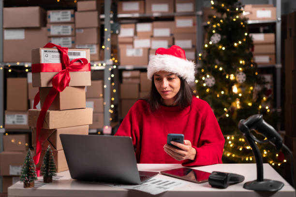 istock Warehouse manager working on christmas uses smartphone and laptop computer, takes orders online, warehouse employee online store in santa claus hat 1704114473