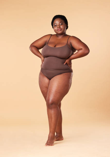 istock Portrait, wellness and plus size with a model black woman posing hands on hips in studio on a beige background. Beauty, underwear and natural with a female sitting on a stool for body positivity 1704132384