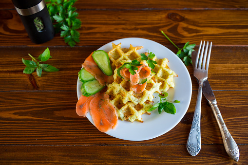 Cooked potato waffles with lightly salted red fish and herbs in a plate, on a wooden table.