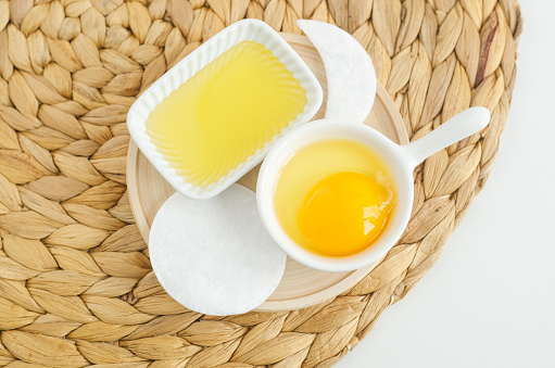 Small white bowl with raw egg and cotton pad. Ingredient for preparing homemade hair or face mask. Natural beauty treatment and spa recipe.