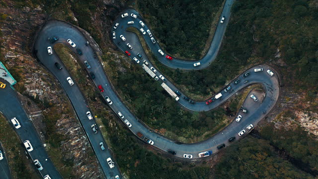 Traffic jam on road in mountains, aerial top down view. Curved narrow road in mountains filed with cars and trucks waiting and slowly moving in traffic jam