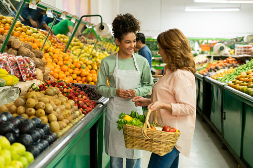 Happy retail clerk helping a woman shopping at the supermarket and smiling - grocery shopping concepts