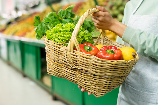 Close-up on a retail clerk holding a shopping basket with fruits and vegetables at the supermarket