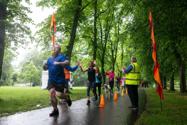 A group of run participants taking part in a fun run in Leazes Park in Newcastle upon Tyne, North East England. Some of them are crossing the finish line and celebrating with their arms raised as volunteers cheer them on and record times. The race is open to people of all ages and abilities and is also dog friendly.\n\nThese files have similar videos/images available.