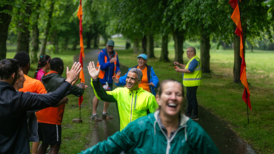 A group of run participants taking part in a fun run in Leazes Park in Newcastle upon Tyne, North East England. Some of them are crossing the finish line and celebrating as volunteers cheer them on and record times. The race is open to people of all ages and abilities and is also dog friendly. One man is hi-fiving the supporters standing at the finish line.\n\nThese files have similar videos/images available.