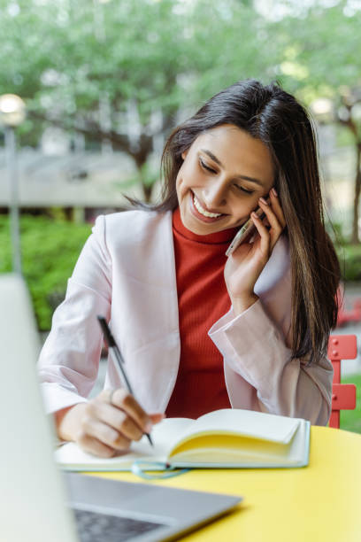 istock Young business woman talking on mobile phone, using laptop computer 1704211044