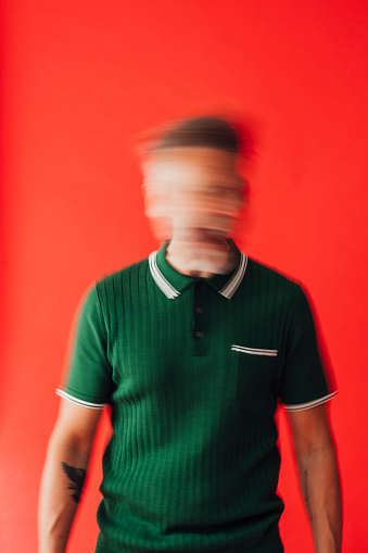 A creative portrait of a young man who has his arms folded and is throwing his head back and forth showing a multiple of emotions which can be interpreted in many ways. He is stood in a studio against a red background in Newcastle upon Tyne in the North East of England