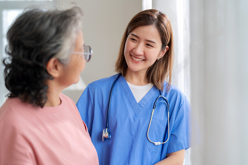Finding Solace and Support: Compassionate Home Healthcare. Dedicated nurse and caregiver stand by the windows with an elderly woman. Her face filled with longing for family, receives heartening encouragement from the doctor by her side. Healthcare and emotional support come together to enrich the retirement years.