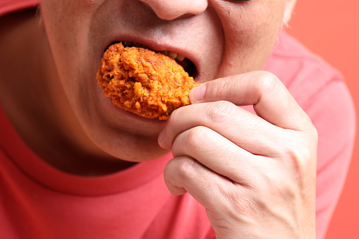 The Asian man eating deep fried chicken on the orange background.