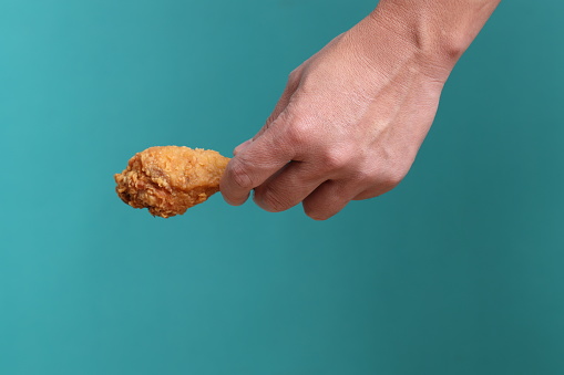 The Asian man hand holding the deep fly chicken fly on the green background.