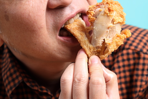 The Asian man eating deep fried chicken on the green background.