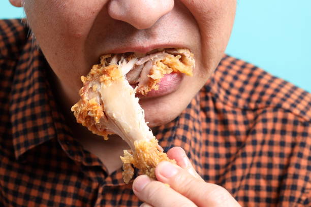 The Asian man eating deep fried chicken on the green background.