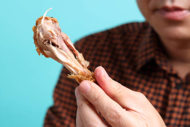 The Asian man eating deep fried chicken on the green background.
