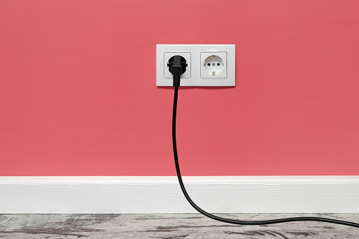 White double outlet installed on pink wall with inserted black electrical plug, front view.