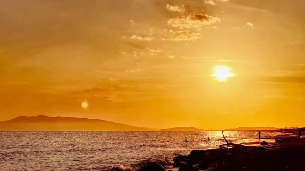 An image of a sunset over the sea on a warm summer day. The sun reflects on the waves, coloring the sky with shades of red and orange.