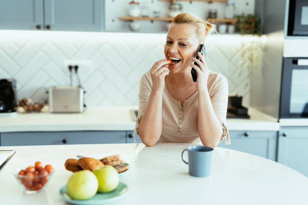istock Mature woman enjoying time at home in kitchen with smart phone, using mobile app 1704291870