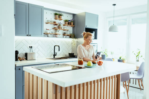 istock Mature woman enjoying time at home in kitchen with smart phone, using mobile app 1704292644